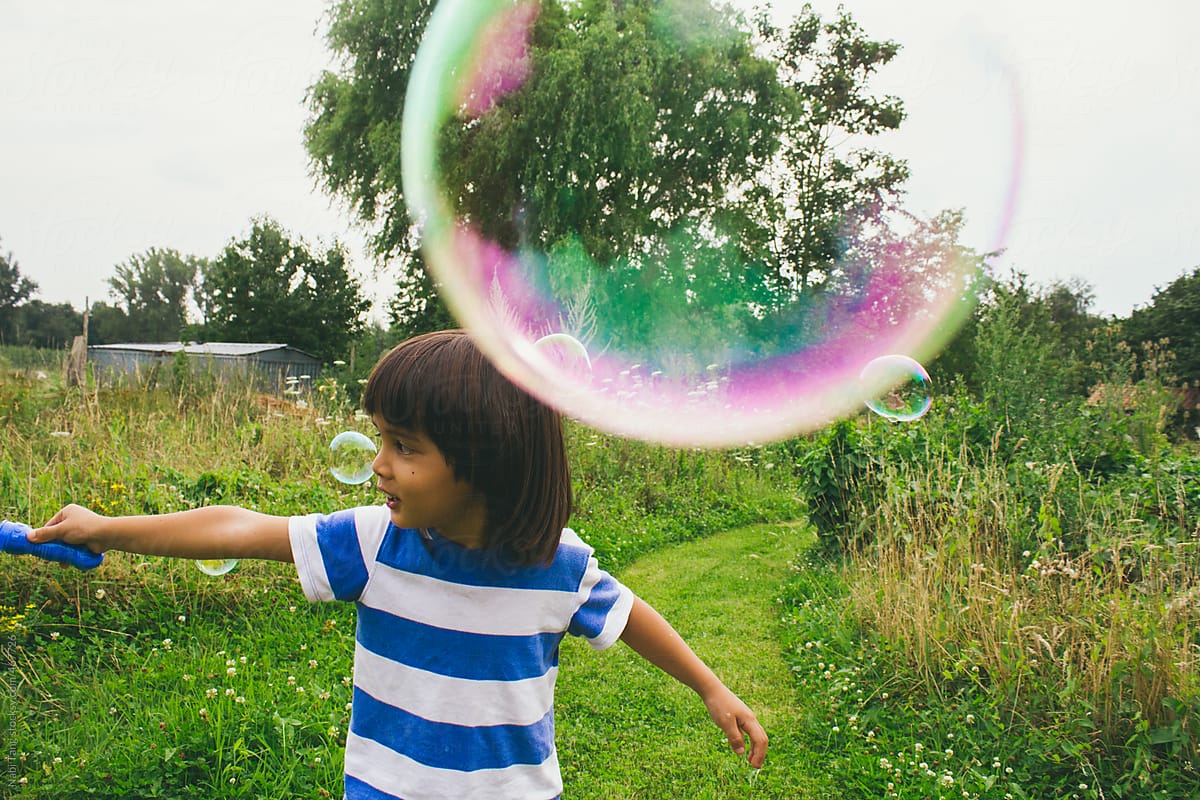 Cute little boy creating huge bubble from a bubble wand in the nature
