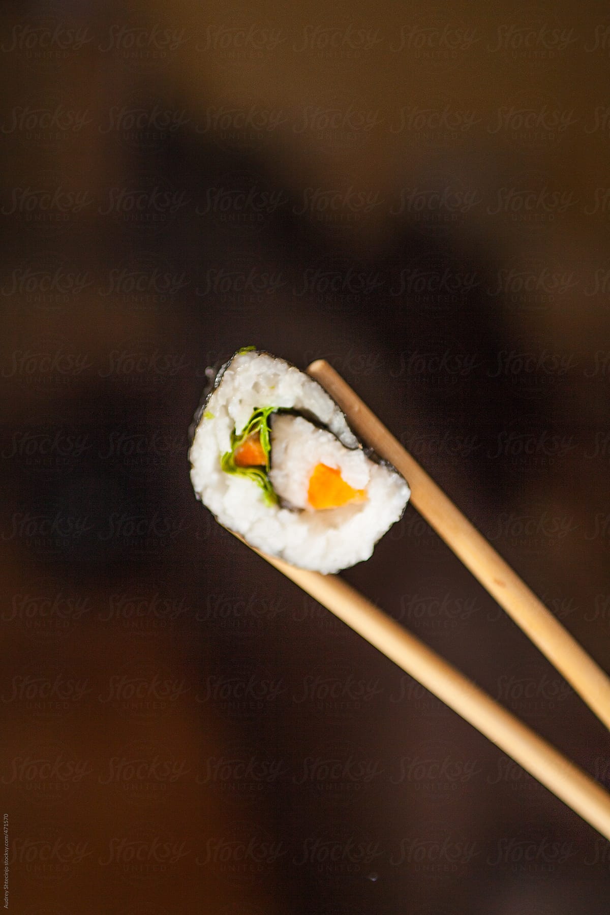 Sushi roll held with chopsticks - close up.