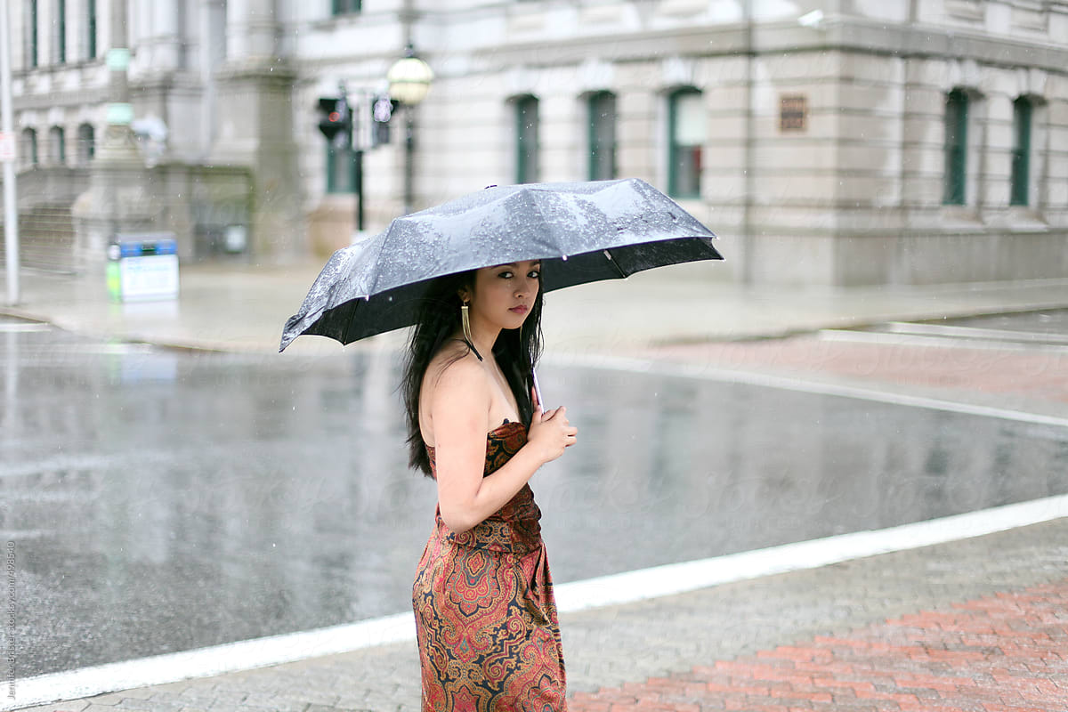 Woman in formal dress standing on a city corner in the rain