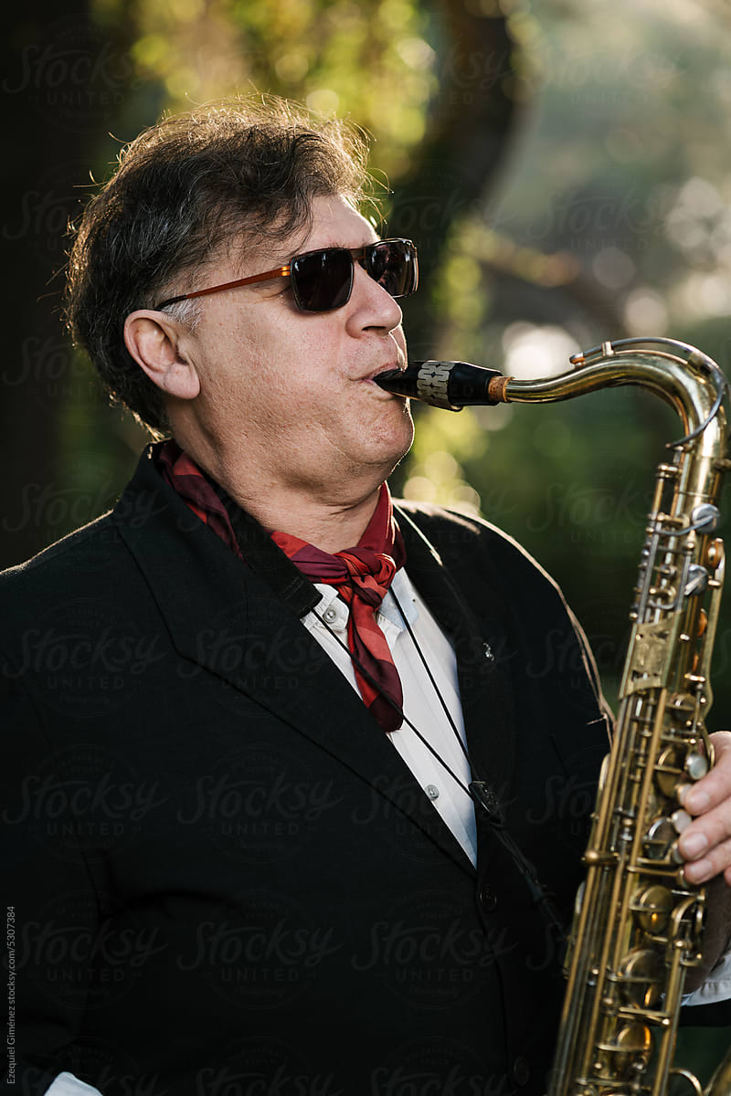 Man in sunglasses playing saxophone on sunny day
