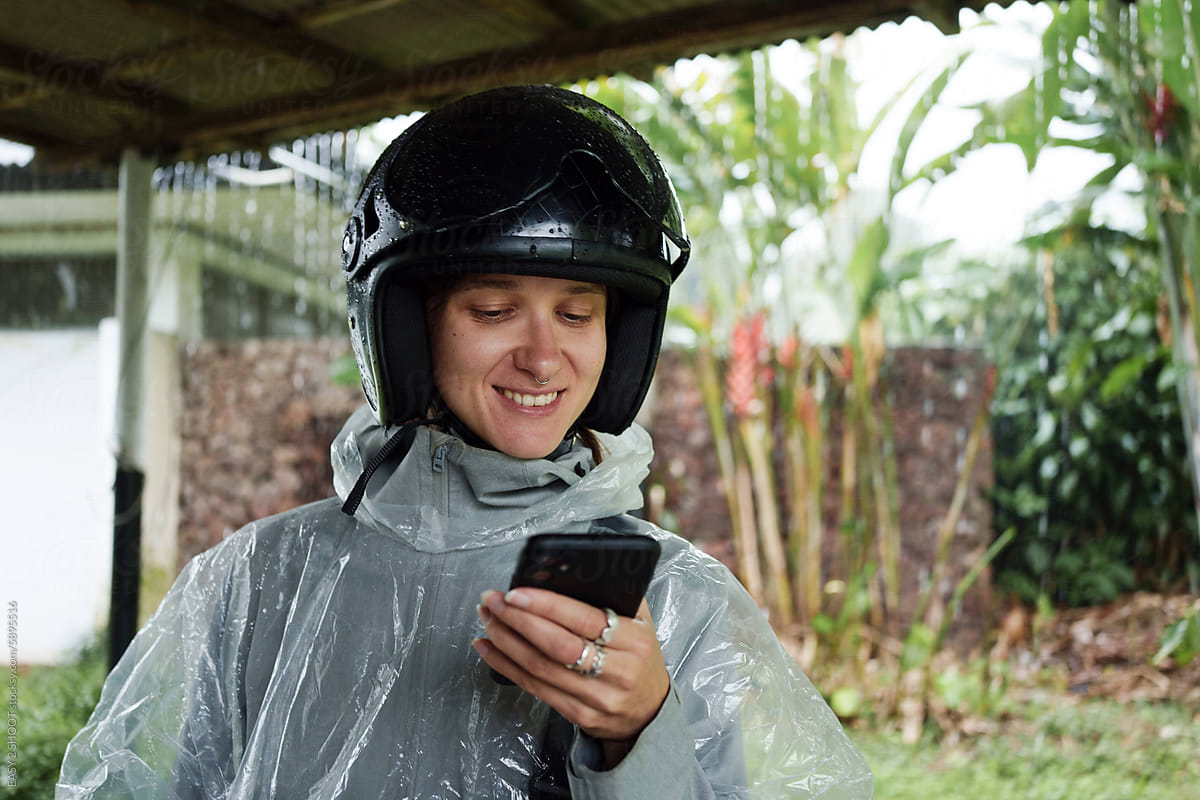 Smiling Person in Rain Gear Checking Phone Under Shelter