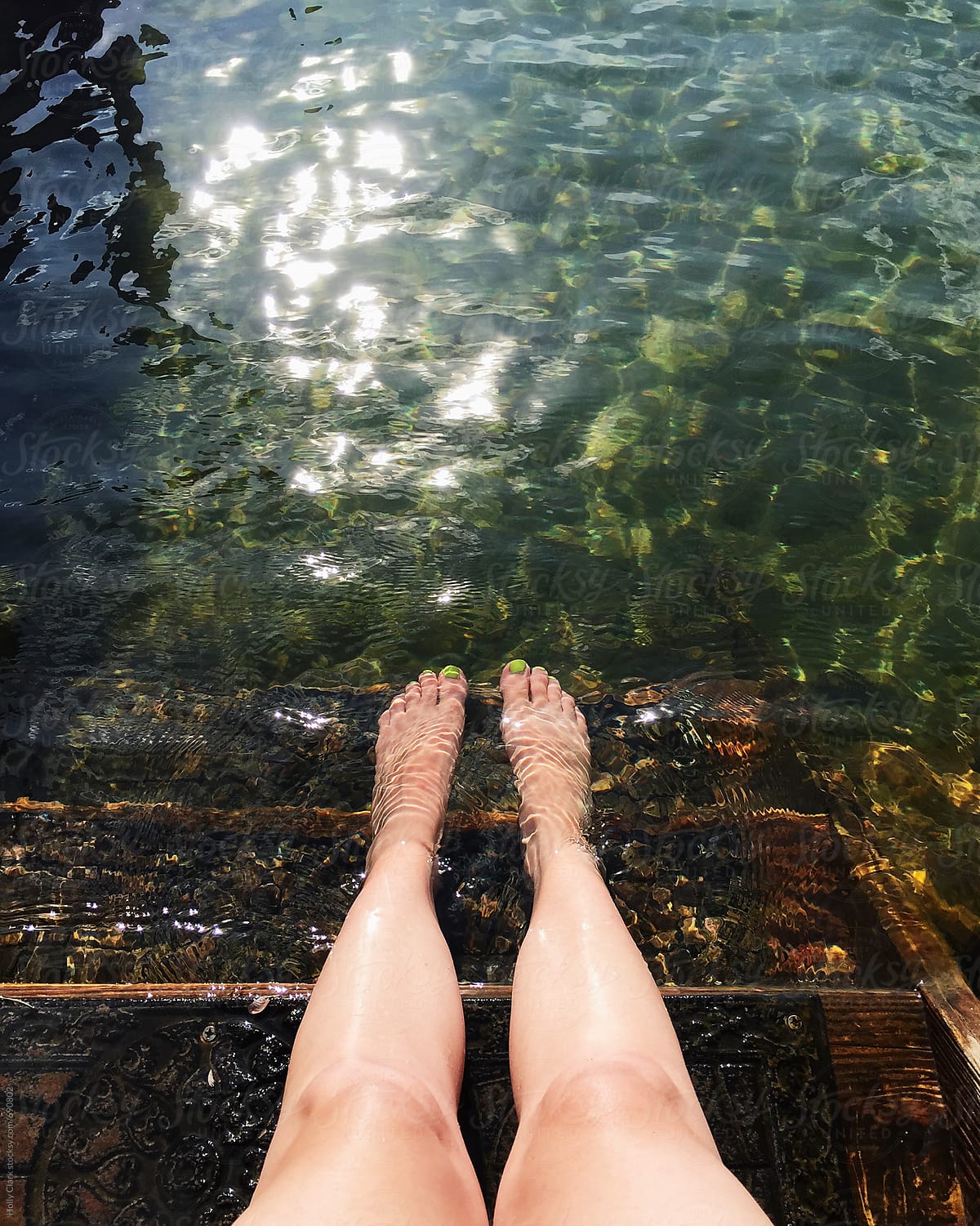 Female feet with green nail polish cooling off in lake
