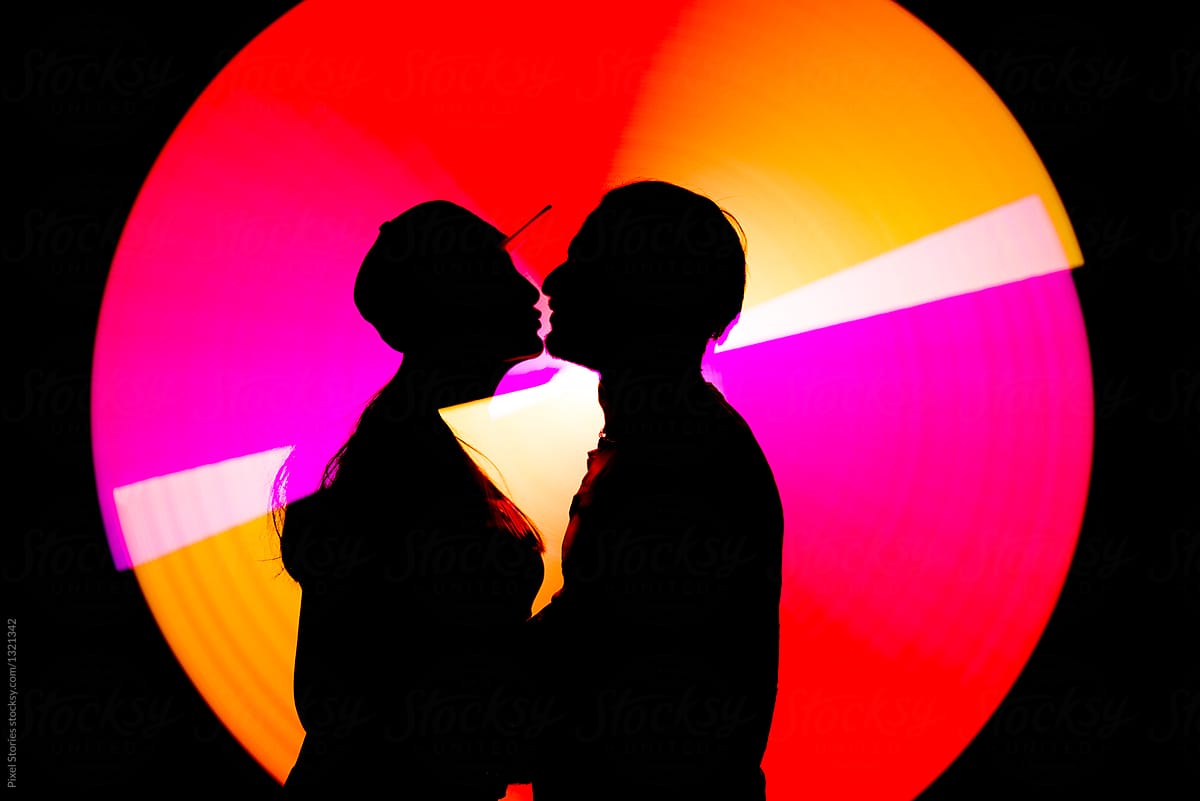 Couple kissing against colorful light