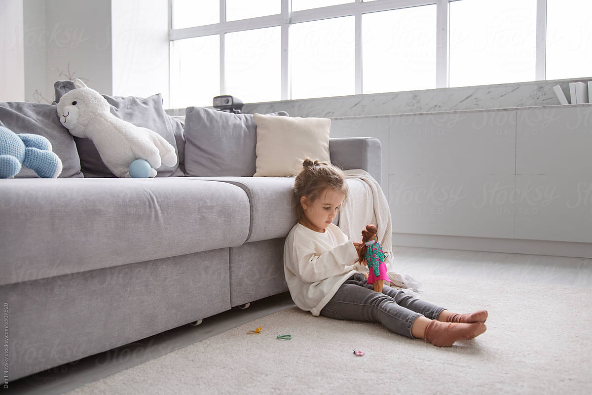 Girl with doll on floor against couch in living room