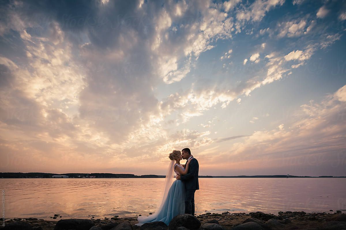 Newlywed couple kissing on nature beach on sunset