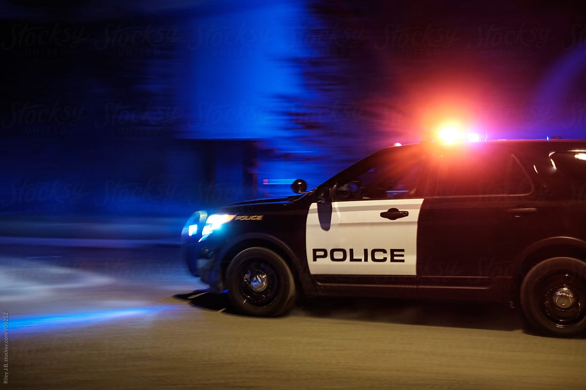 A police vehicle driving fast with red & blue lights flashing.