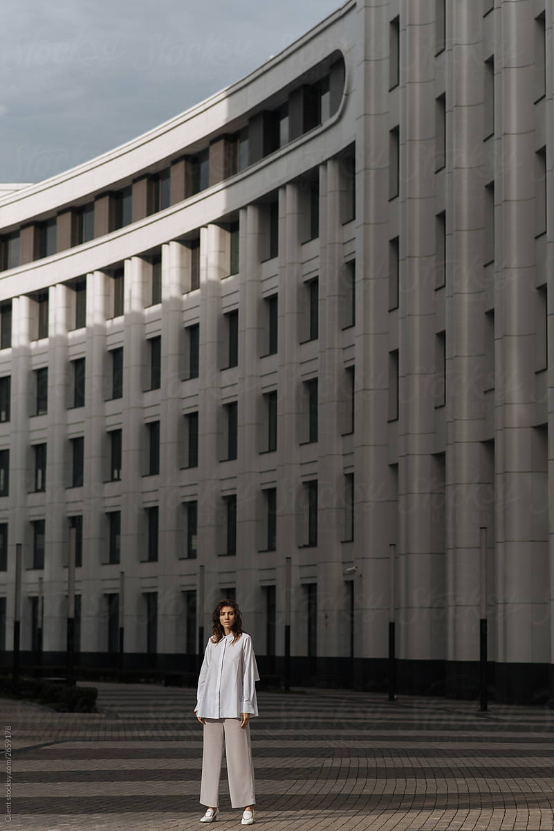 fashion portrait of a girl in a gray sweater and white sheep on the background of modern architecture