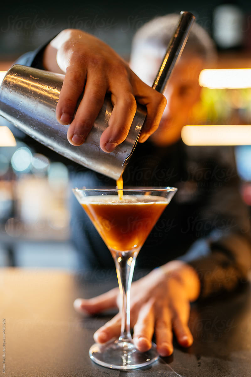 Bartender pouring cocktail into martini glass in bar