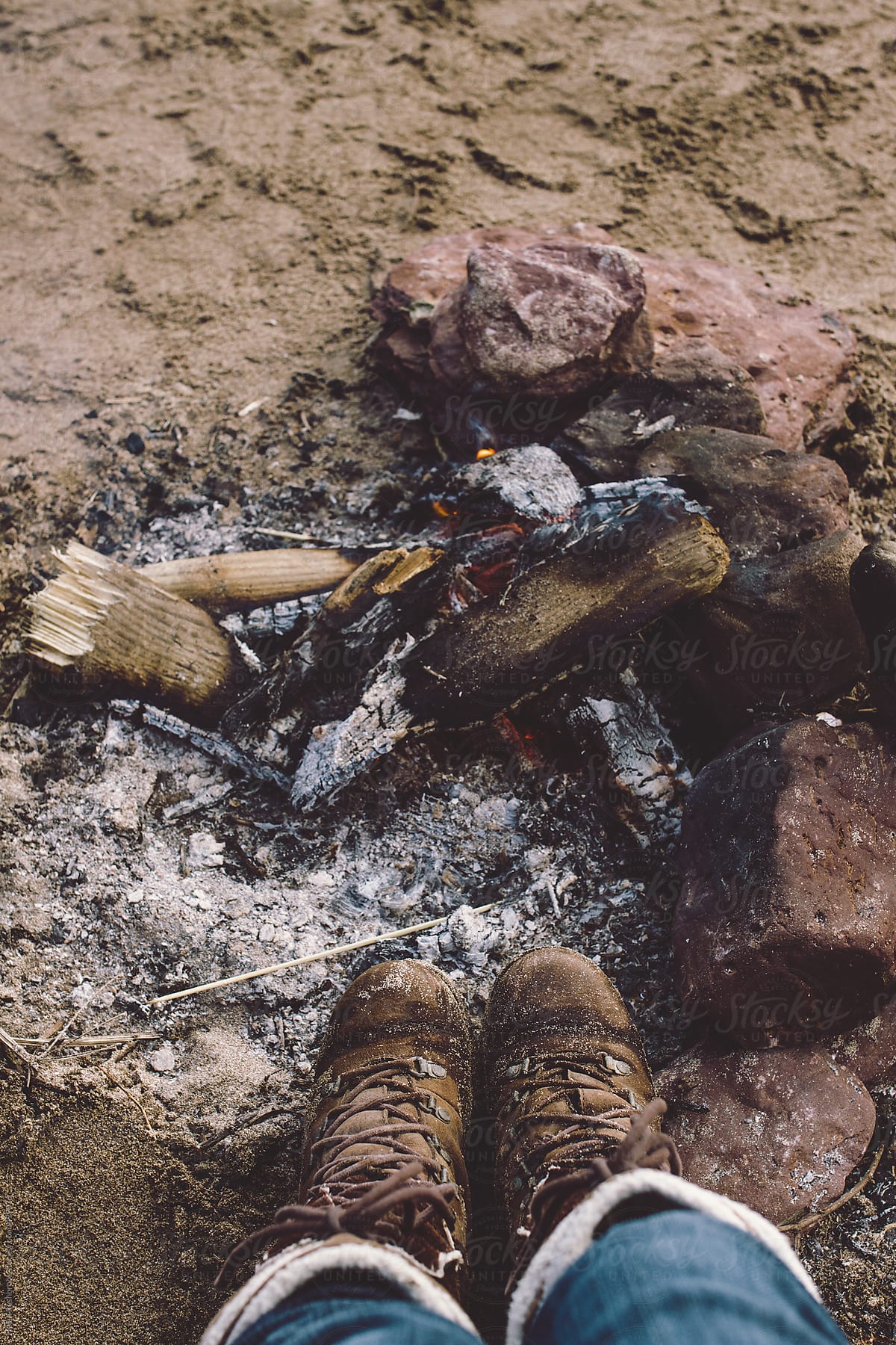 Feet, in boots, warming in front of a fire on a beach.