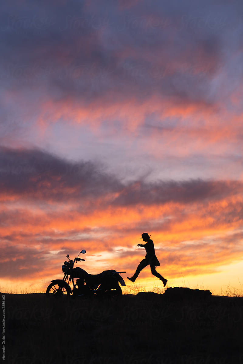 Traveler woman in a hat by the motorcycle at sunset sky.
