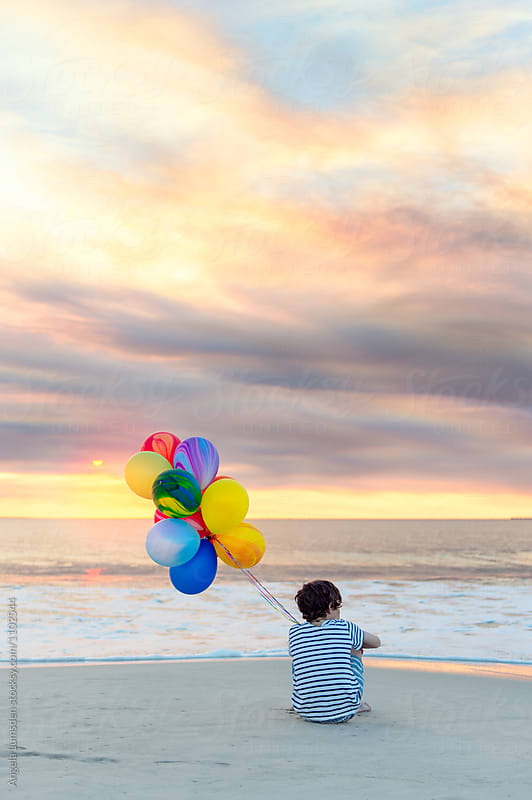 Boy sitting at the beach with a large bunch of colorful balloons