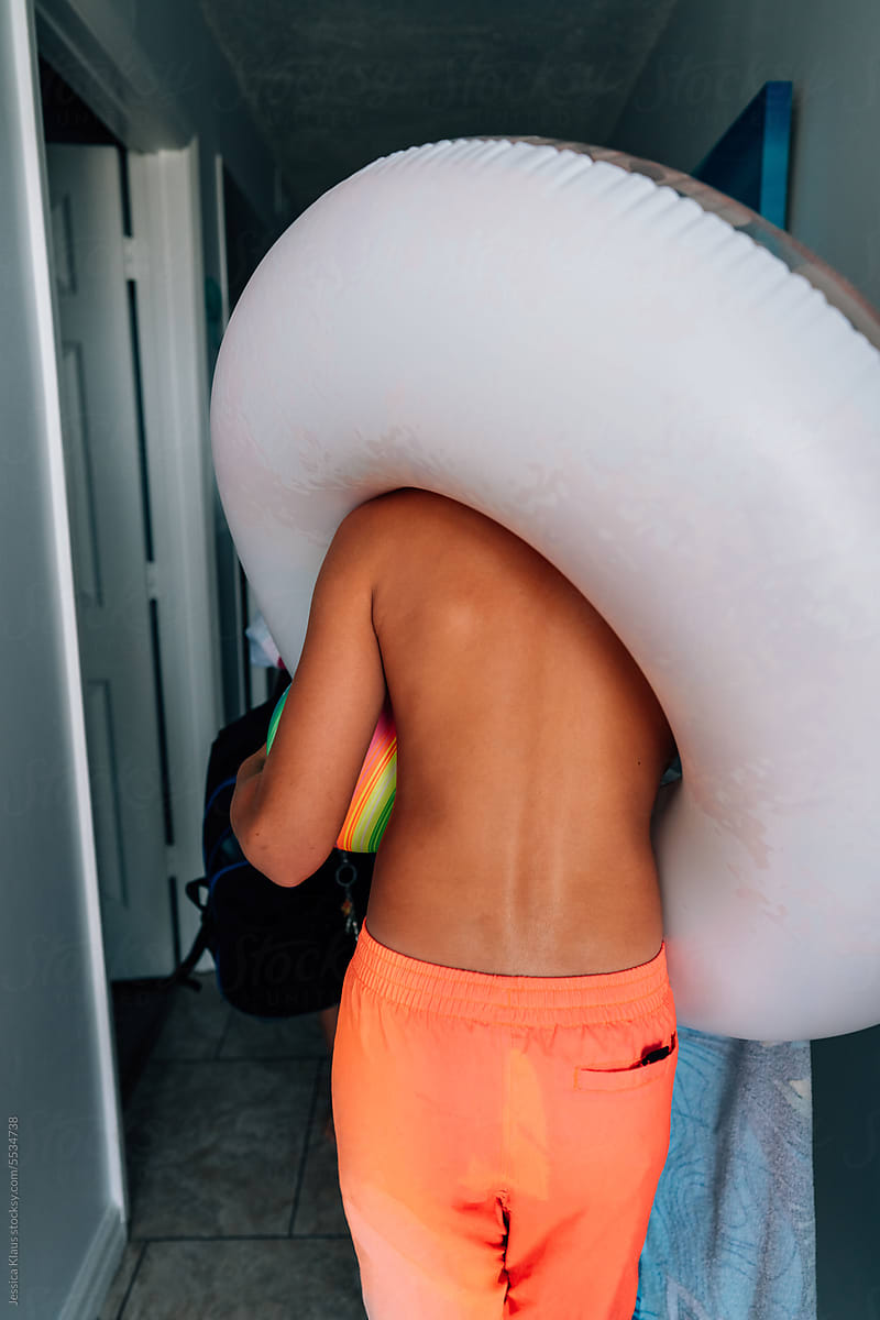 Shirtless male walking with water tube over his shoulder.