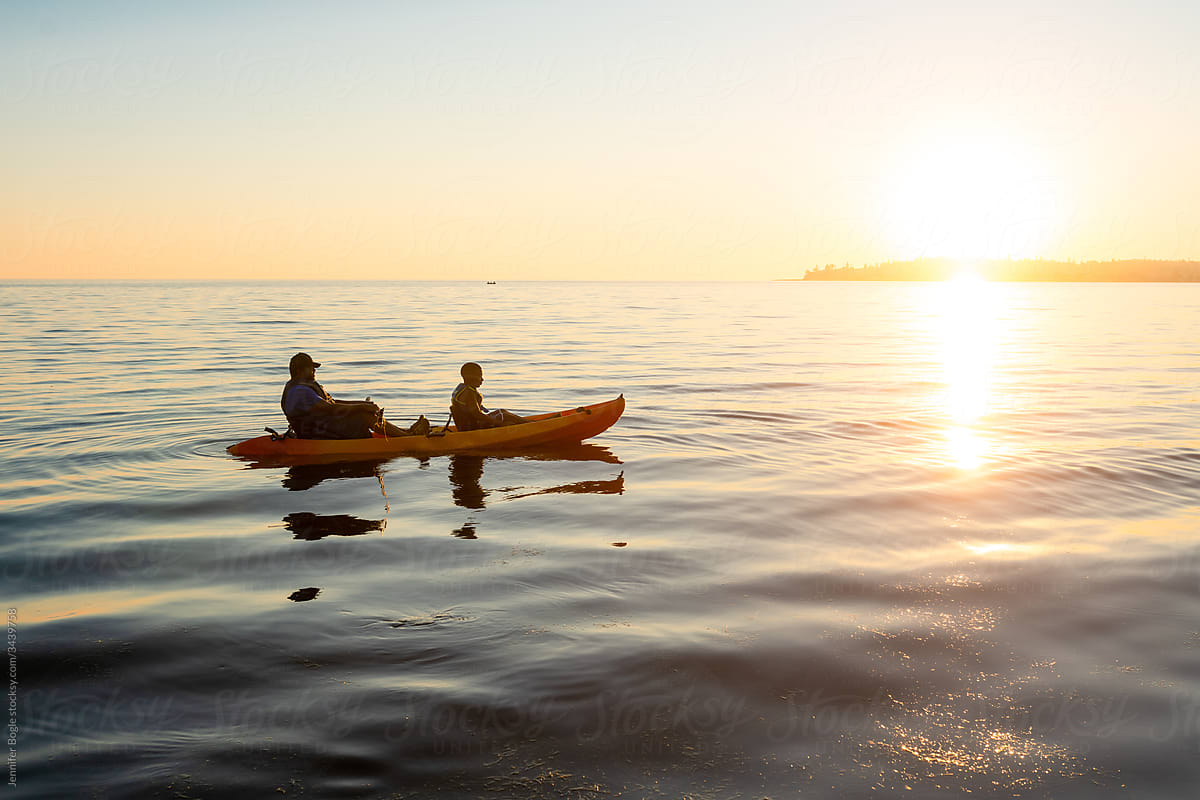 Father and son row in tandem kayak at sunset