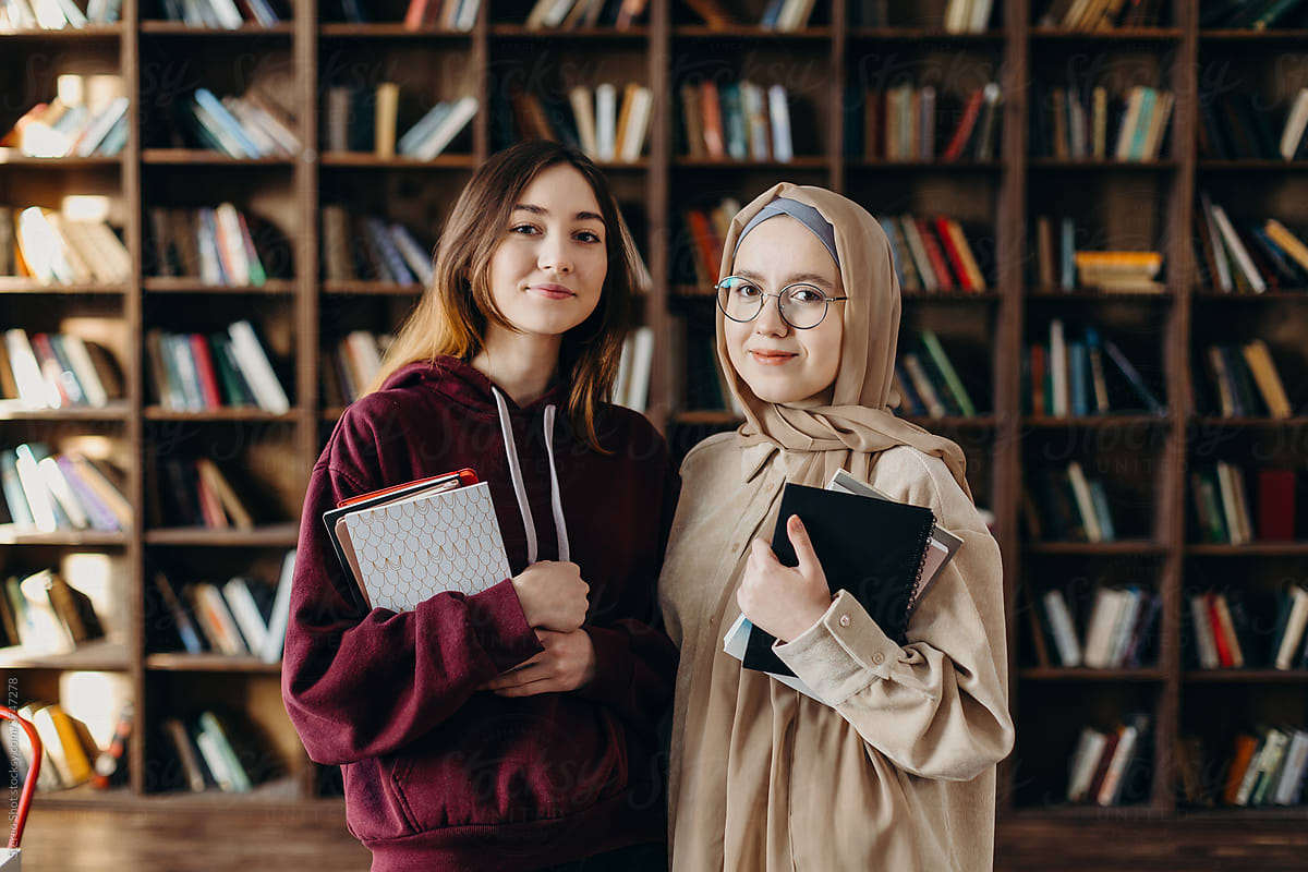 Content diverse female students with textbooks standing in library