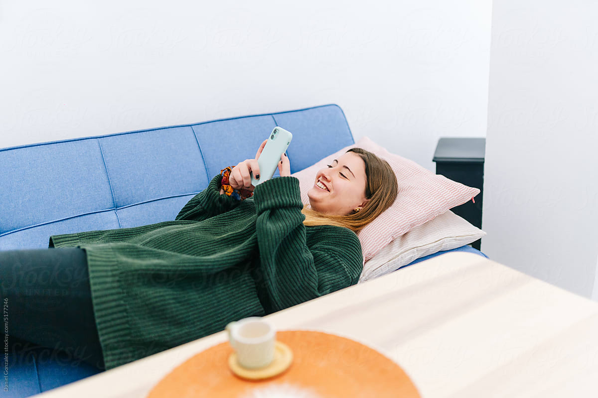 Happy woman lying on sofa with smartphone