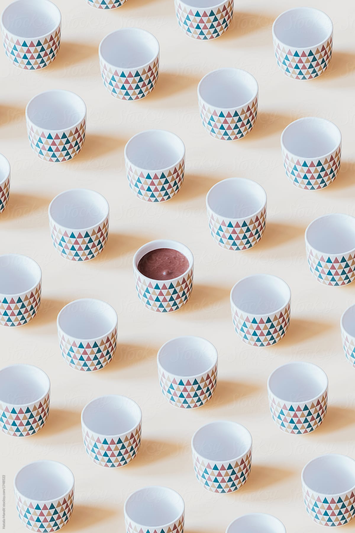 Pattern of empty mugs with just one mug with chocolate
