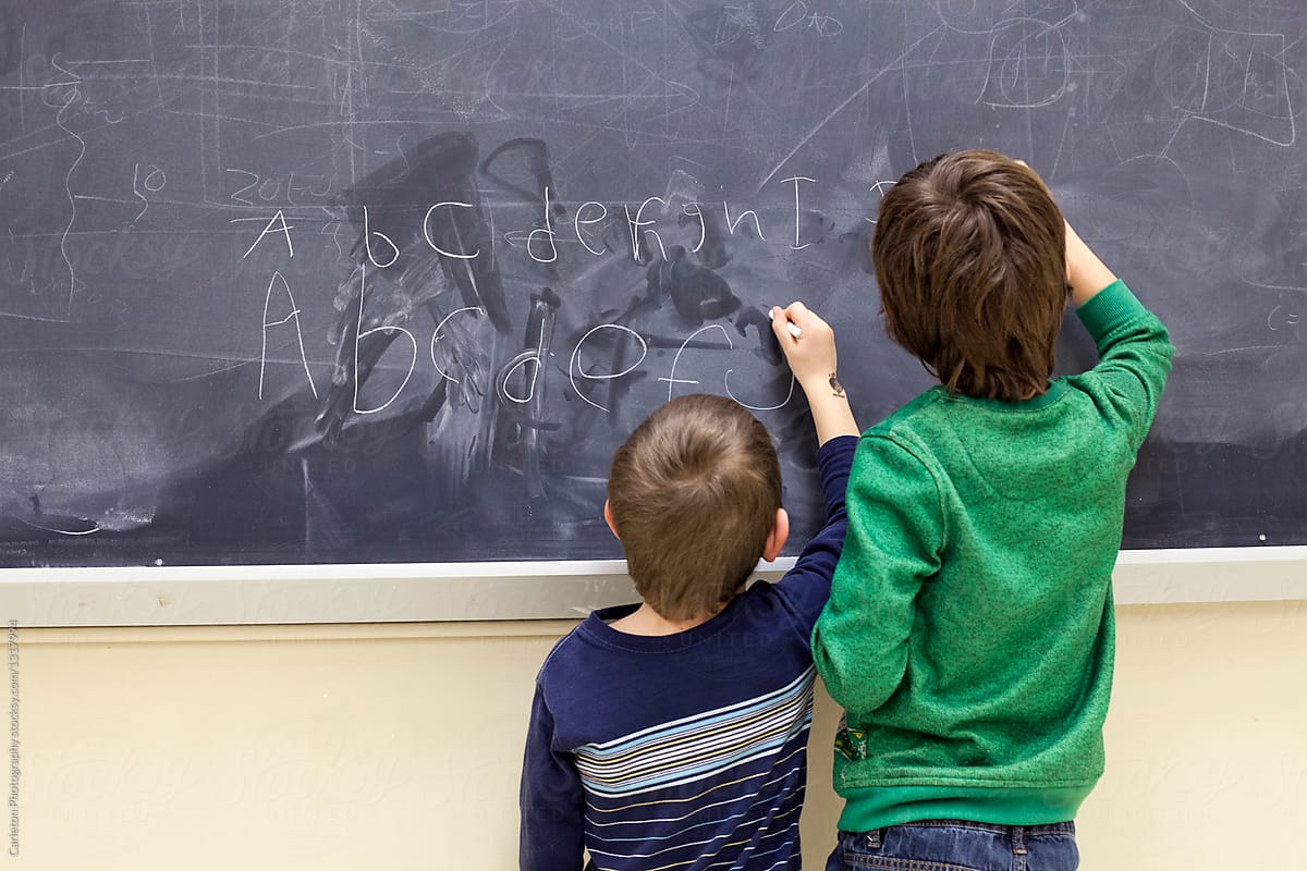 Older brother shows younger brother how to write the alphabet with chalk on a blackboard