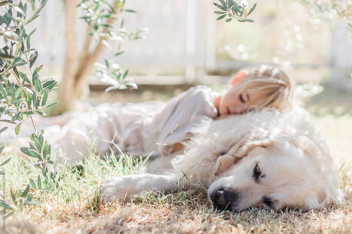 girl sleeps under olive tree while laying on her dog