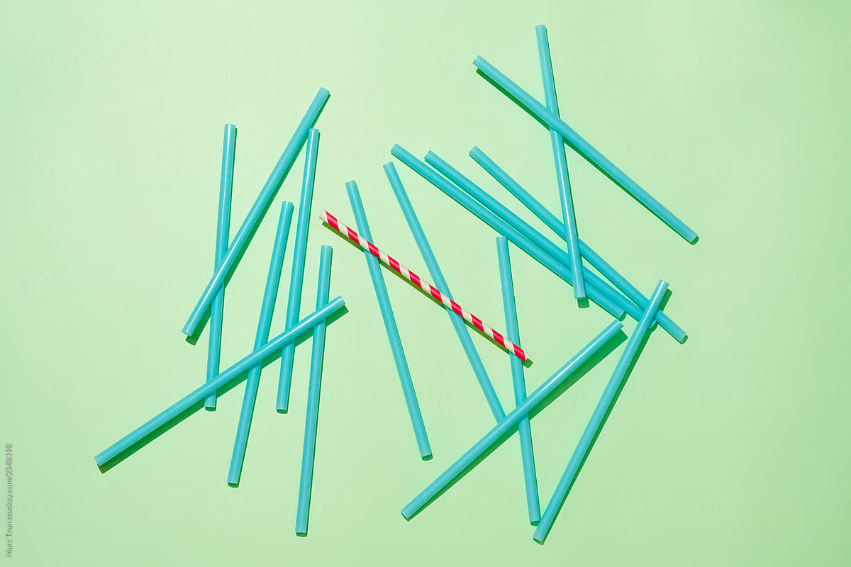 Paper straw among with pile plastic straws on green