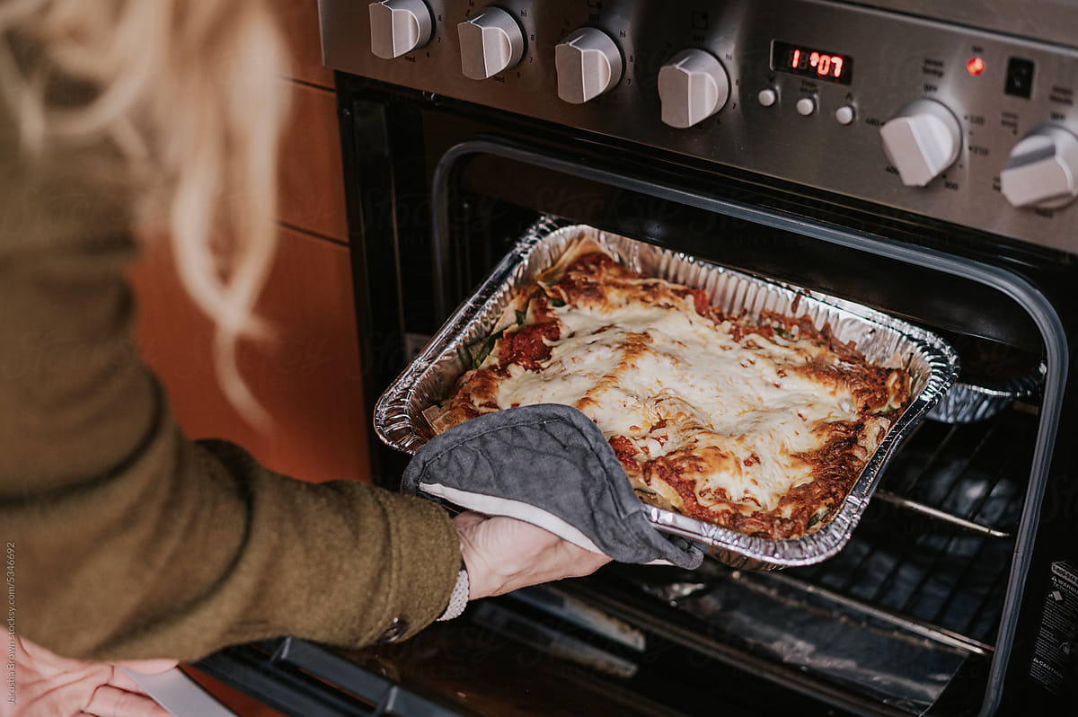 Woman pulls cooked lasagna from oven.