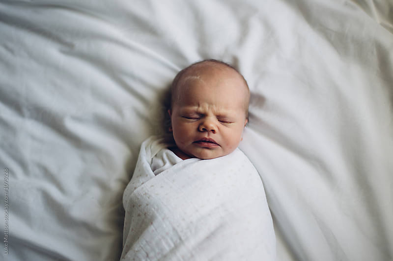 Newborn Baby Girl Swaddled In Blanket Lying On White Sheets