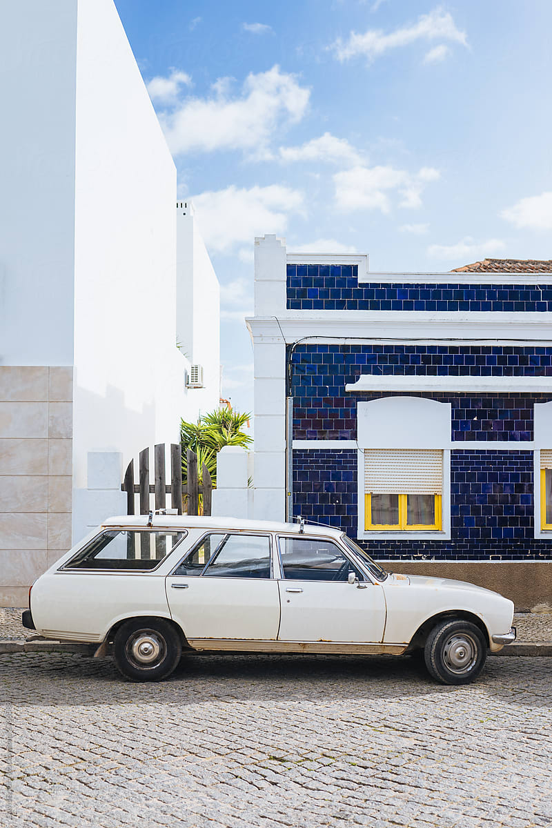 Old white car parked in the street with white and blue buildings in the background