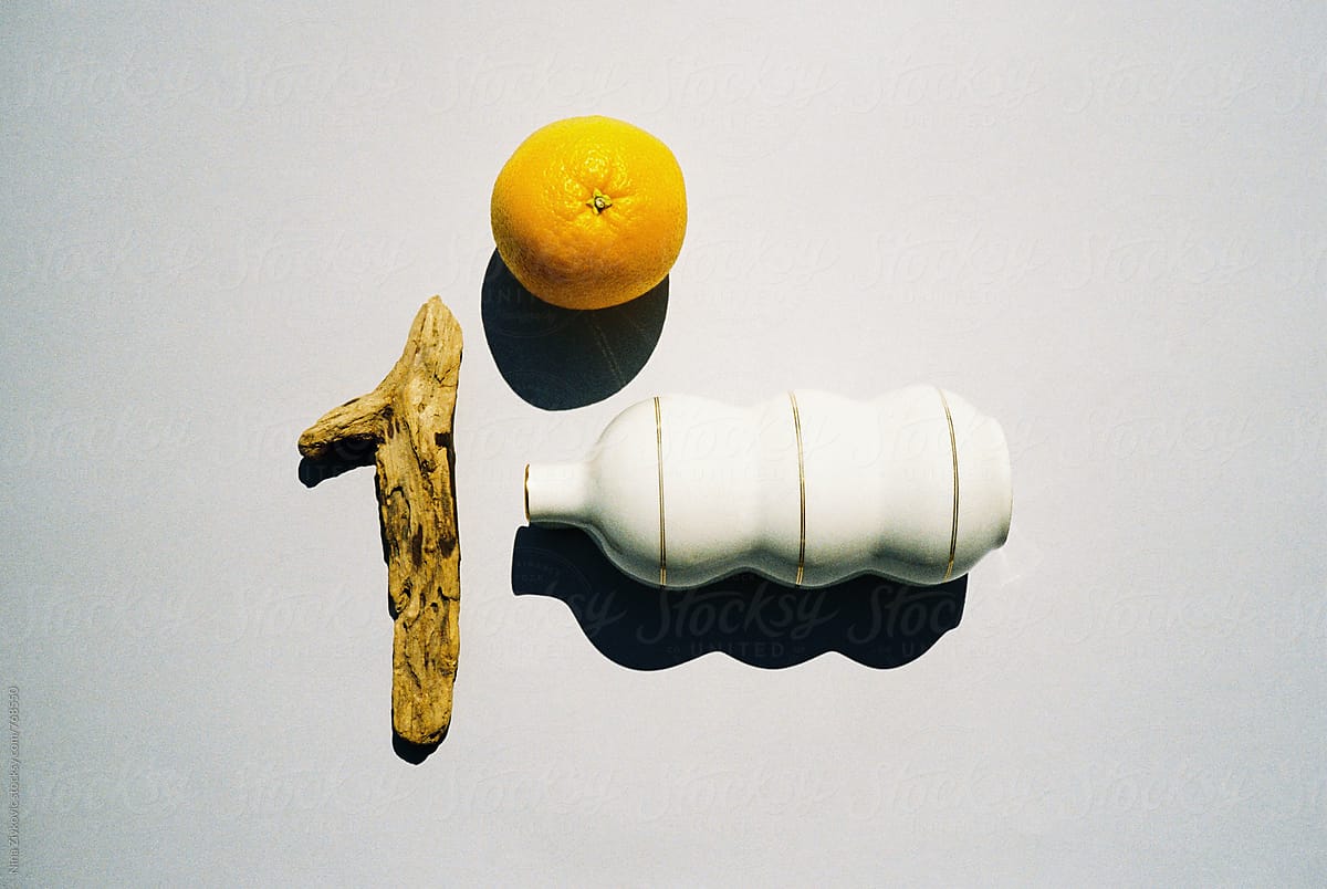 Still life composition with an orange, wood piece and tea pot.