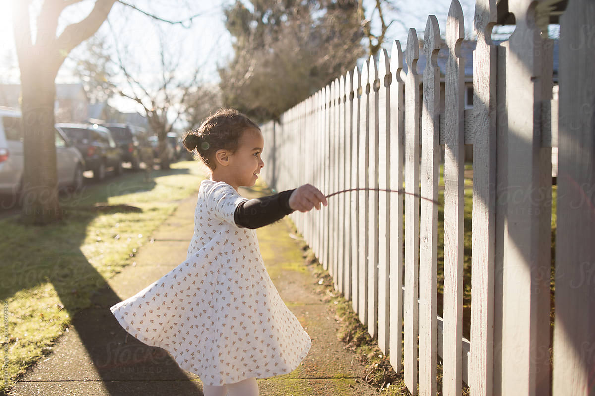 Girl runs stick along picket fence