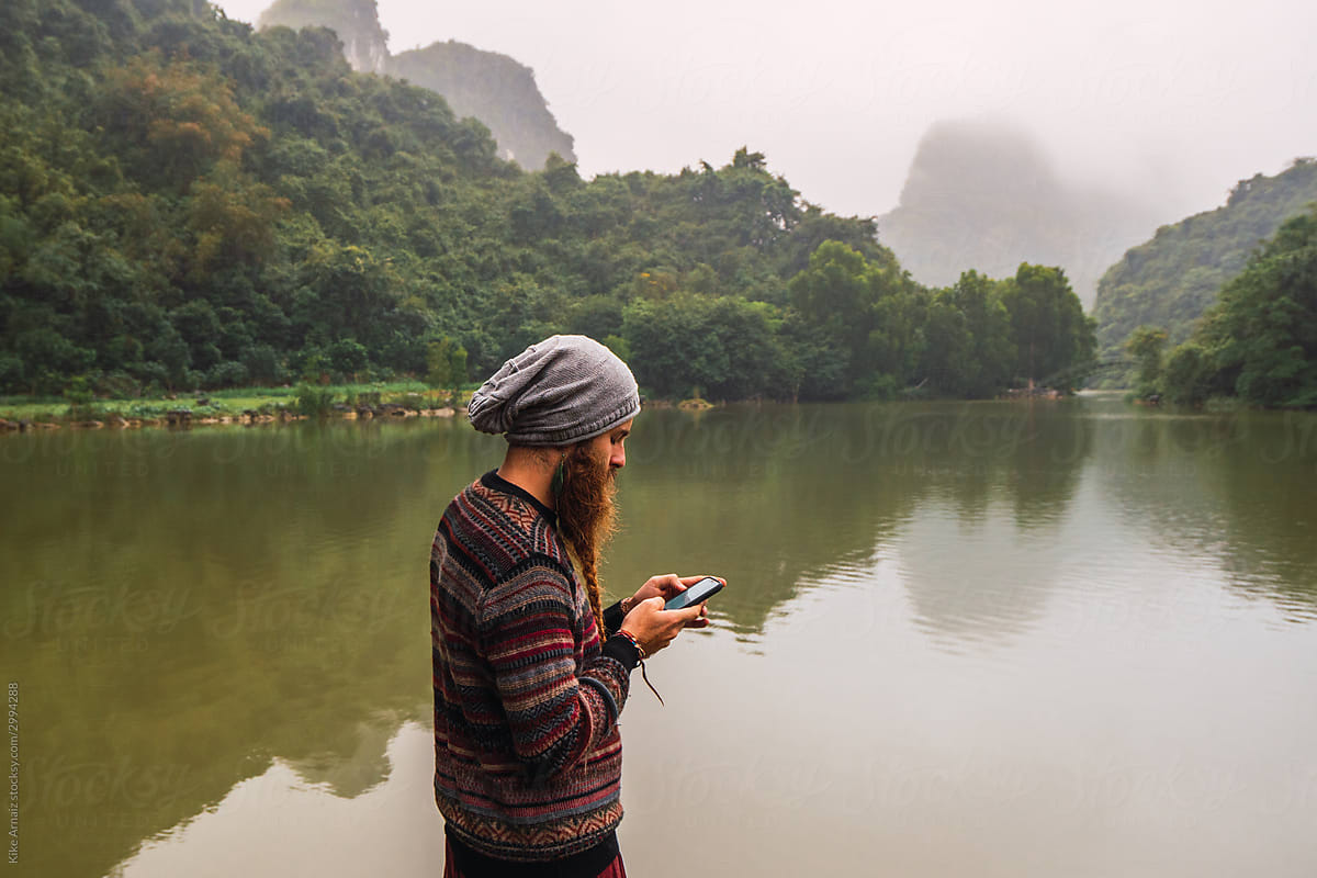 Man using his cell phone in a river with the mountains reflected