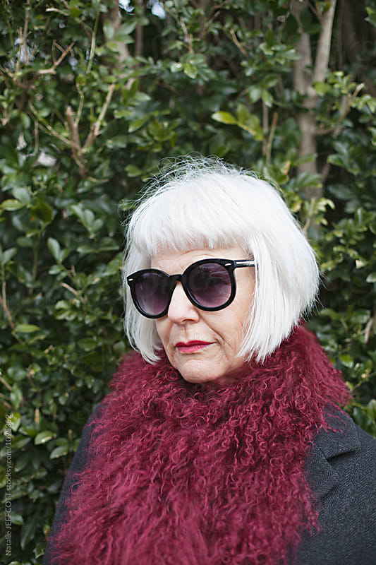 stylish and attractive older woman outdoors wearing a scarf and sunglasses