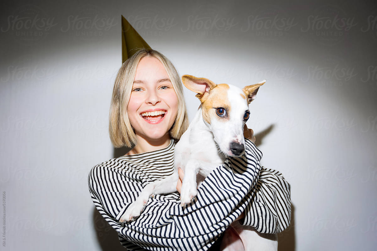 Young Woman In A Party Hat Hugging A Dog And Smiling