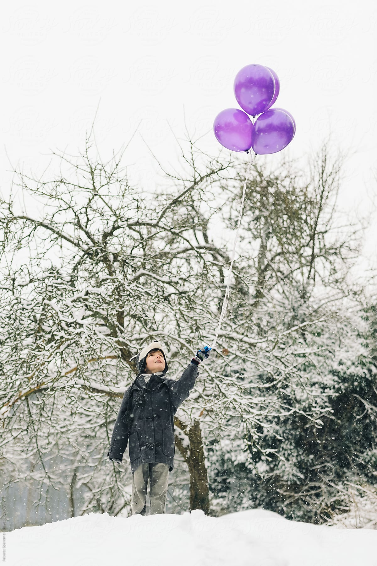 Child in snow holding purple balloons