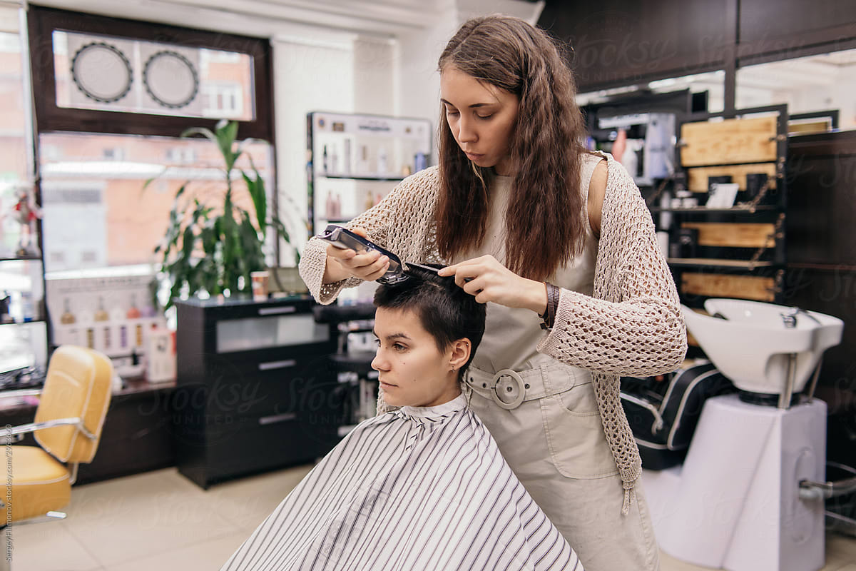 Female hairstylist trimming hair of androgynous client in salon