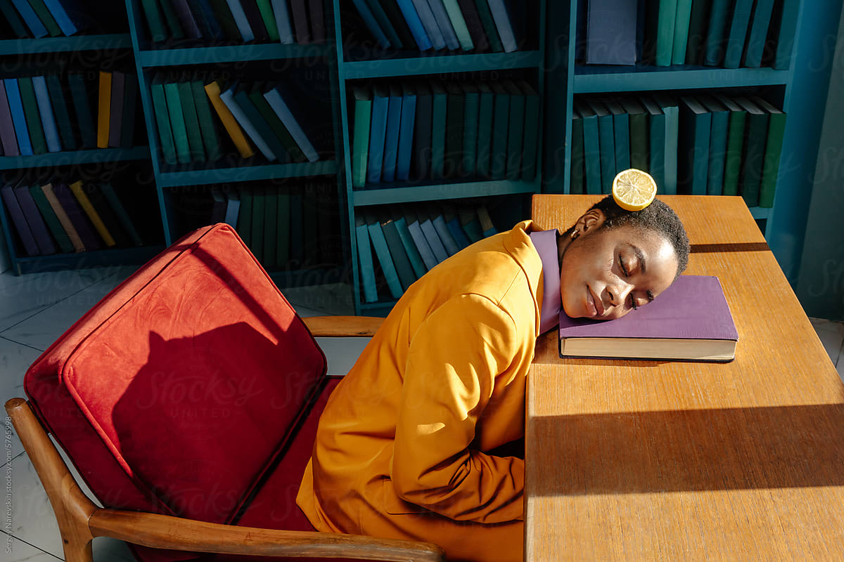 Woman in library sleeping on book, cutted lemon on hair