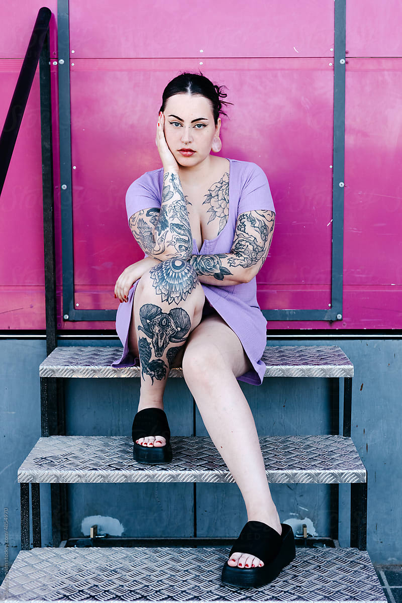 Tattooed brunette sitting on steps and touching face