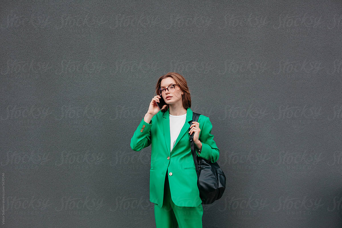 Young woman in elegant suit with backpack, talking on the phone