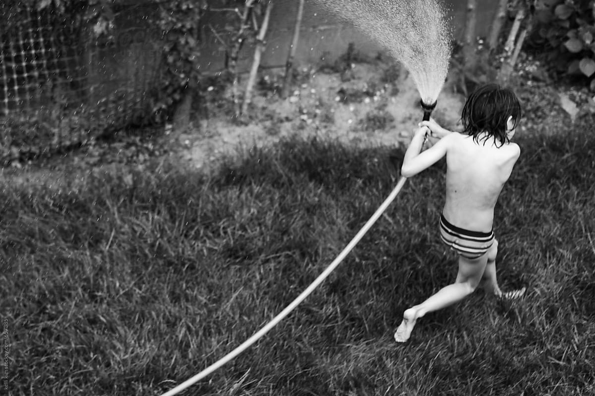 black and white image of boy playing with hose in yard