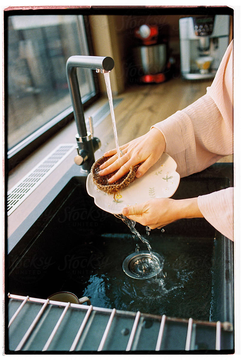 Closeup of anonymous female hands washing dishes in a cozy kitchen