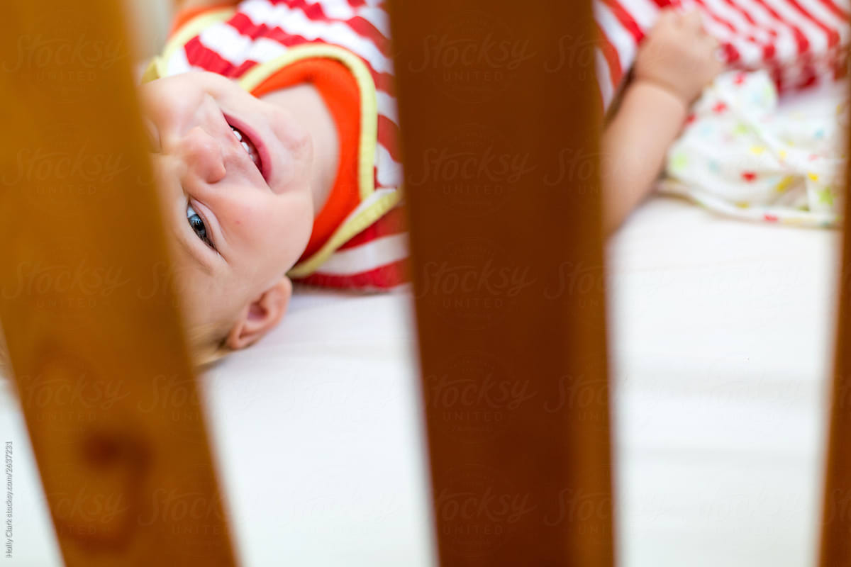 Happy boy looks up through wooden bars of crib