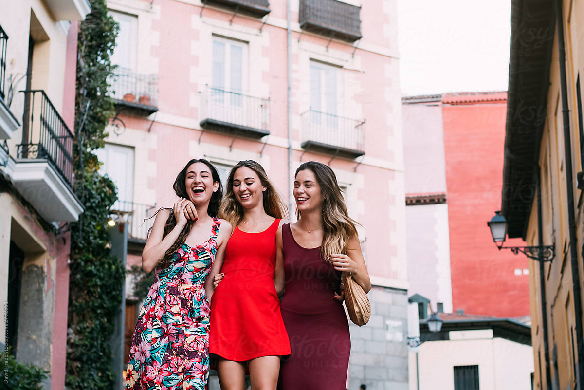 three women waking and laughing in a picturesque street in a summer evening