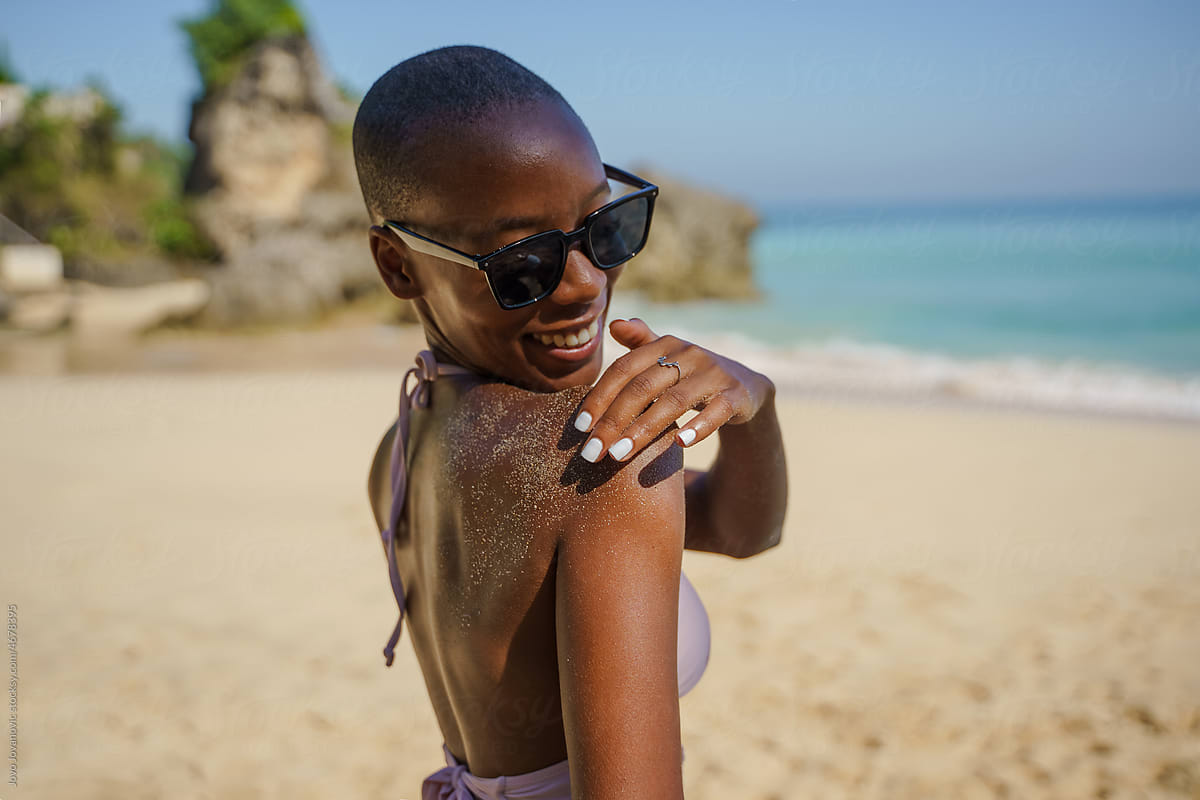 Happy African American woman brushing off sand from body at beach