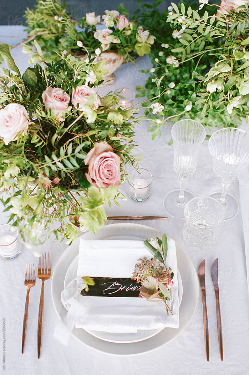 From above an elegant wedding reception tabletop with overgrown greenery, soft copper accents and pink florals