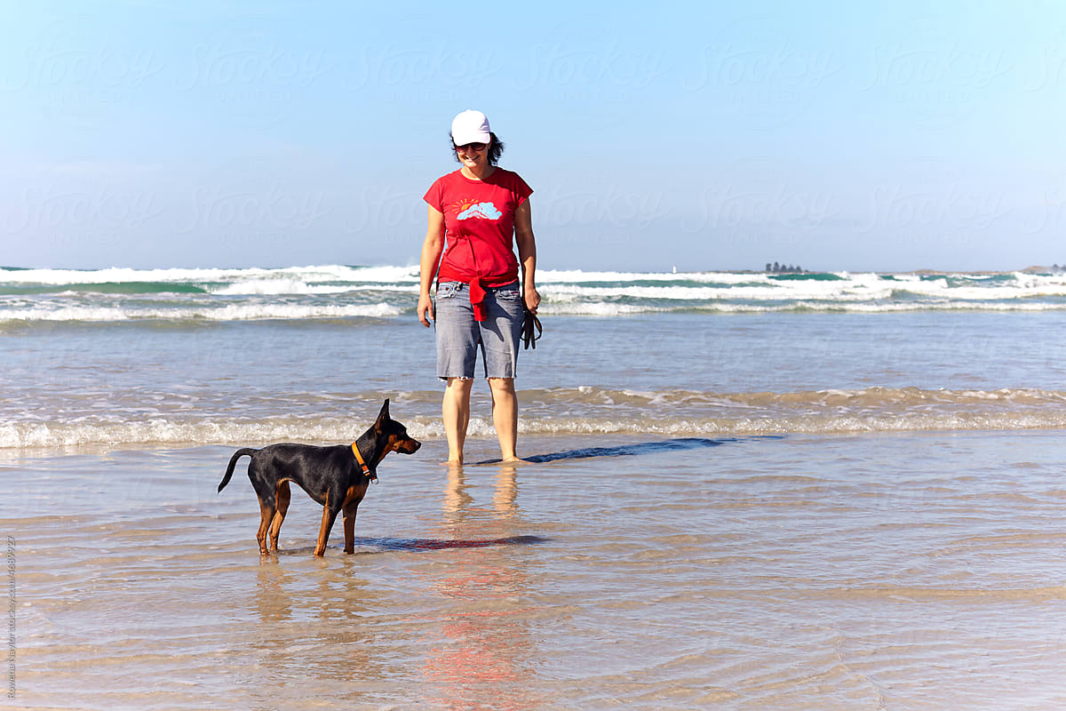 Woman and pet dog stand in ocean