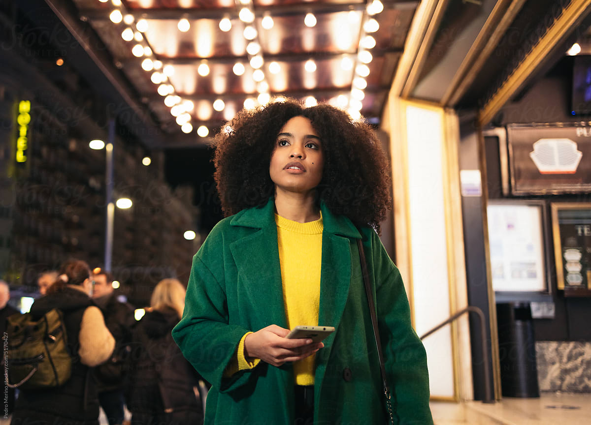 Black woman using smartphone waiting at the theater the city at night