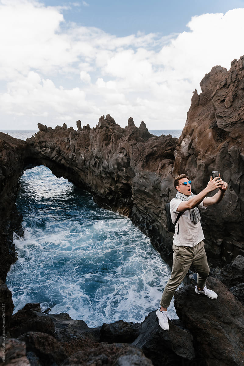 Male tourist taking selfie near natural arch from stone.