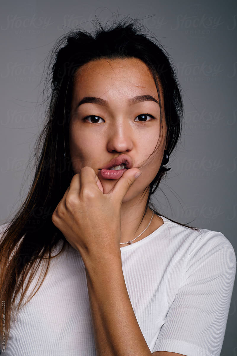 Young Asian girl making faces with hand at lips