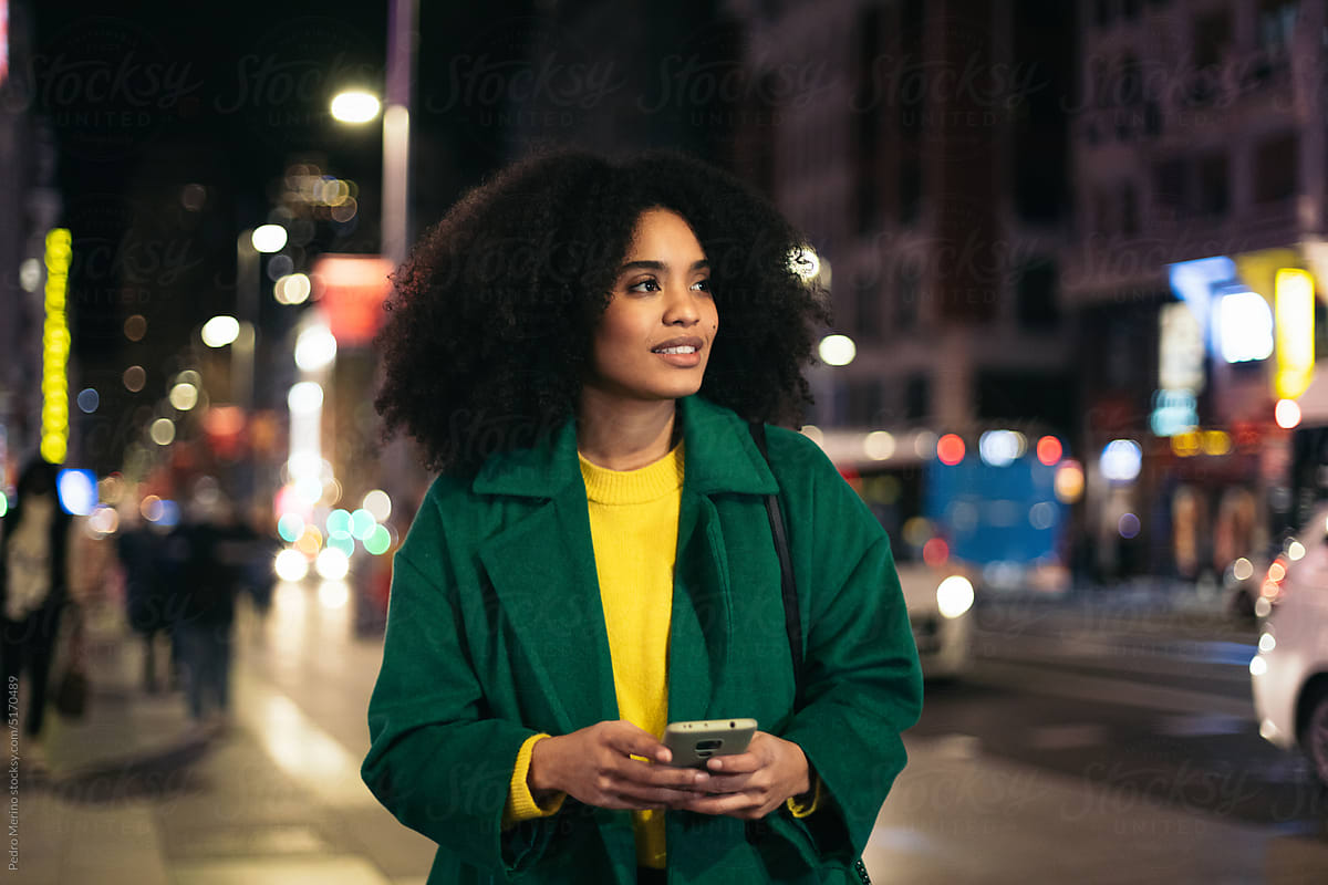 Black woman using smartphone walking through the city at night