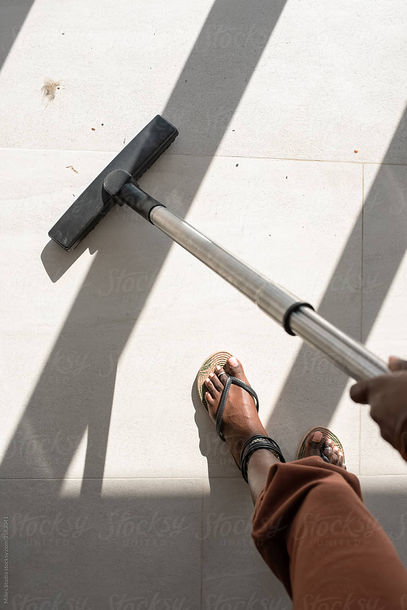 Crop black housewife vacuuming tiled floor