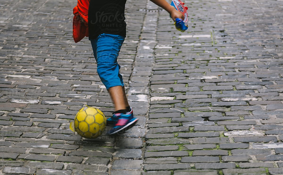 Child Playing Soccer in a Cobblestone Street