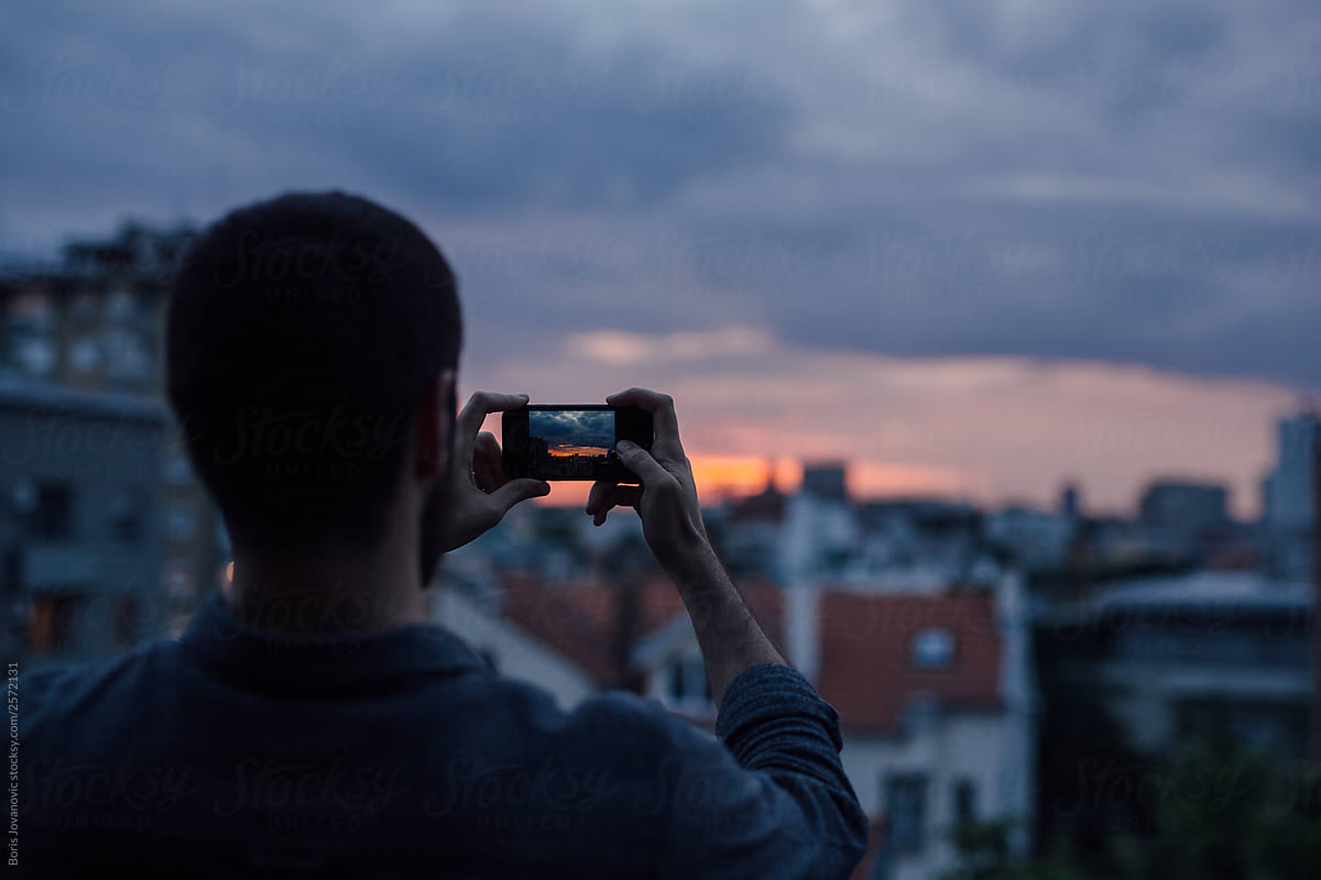 Man photographing a sunset above city